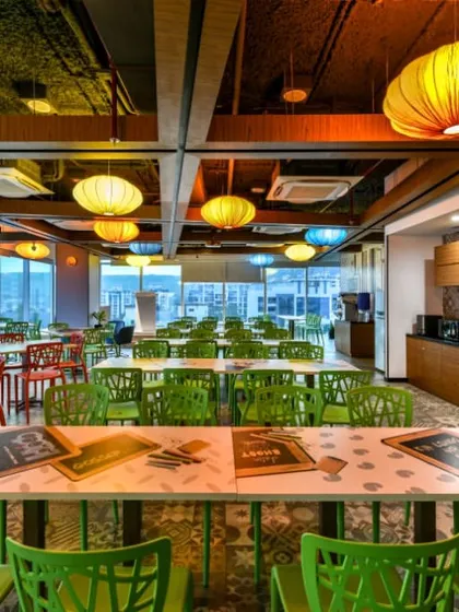 A colorful cafeteria with bright green and red chairs and multi-colored paper lanterns hanging from the ceiling. The space has large windows that offer great views and natural light.