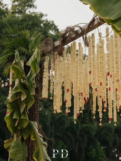 The texture and detail of a South Indian wedding mandap, featuring rustic vines and fragrant tuberose garlands against a backdrop of banana leaves.