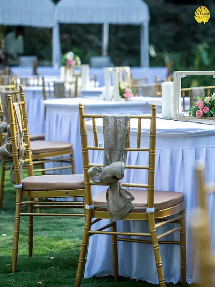 A close-up of a simple, elegant outdoor table setting. The white linens and rustic chair decor create a clean and sophisticated look for a daytime event.