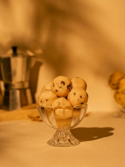 Edible cookie dough balls served in a vintage glass, with warm, dappled light creating a cozy, evening mood. This shot is all about capturing a feeling of comfort and indulgence.