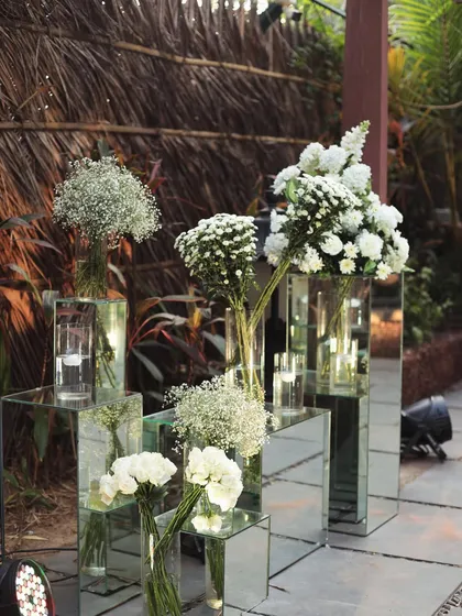 Mirrored pedestals with white floral arrangements add a touch of modern elegance to the rustic beach setting.