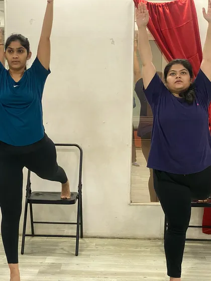 Two members practicing a balancing pose, showcasing the supportive and communal nature of our classes.