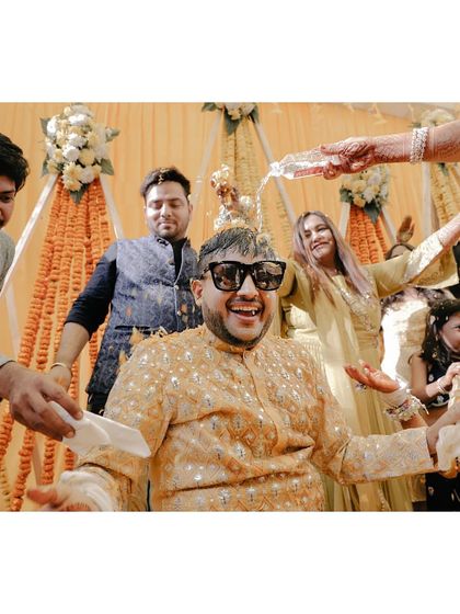 The groom laughs as he's showered with water and petals, wearing sunglasses for a cool, fun look.