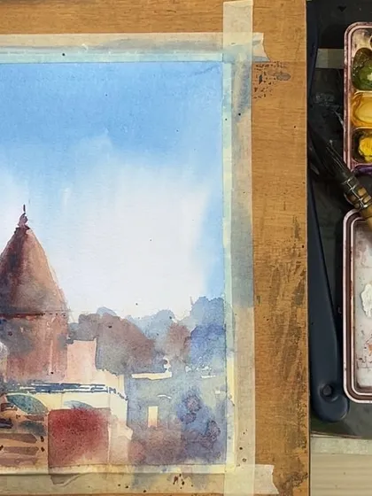 A work-in-progress shot of a Varanasi cityscape. You can see my watercolour palette and brushes next to the painting, showing how I build up layers of colour to create the final scene.