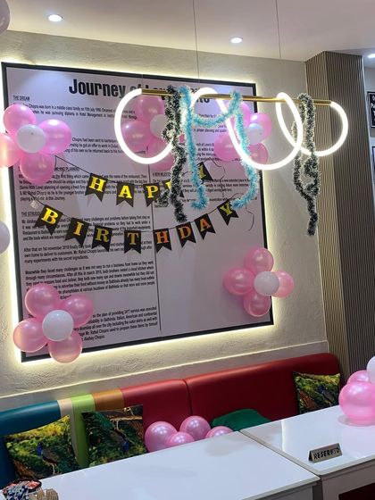 A simple birthday decoration setup at a cafe. We used pink and white balloon clusters and a 'Happy Birthday' banner to create a celebratory atmosphere for a small party.