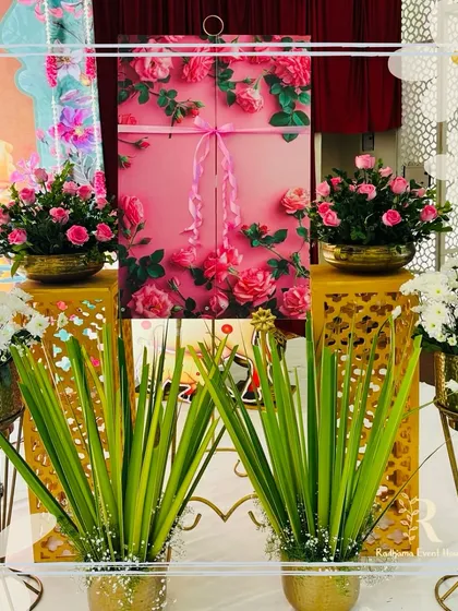 A beautiful name reveal box for a naming ceremony. The pink box, adorned with a rose pattern and a ribbon, is surrounded by fresh flowers in golden pots, creating an elegant and exciting way to announce the baby's name.