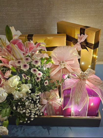 This view shows the beautiful contrast between the shimmering gold gift boxes and the soft pink wraps. The entire hamper is brought to life with fresh flowers and the magical sparkle of fairy lights.