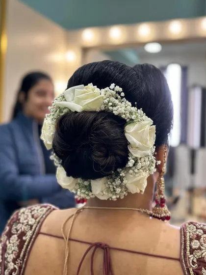 A classic bridal bun surrounded by a full gajra of white roses and baby's breath. This is a timeless and fragrant choice for a traditional wedding ceremony.