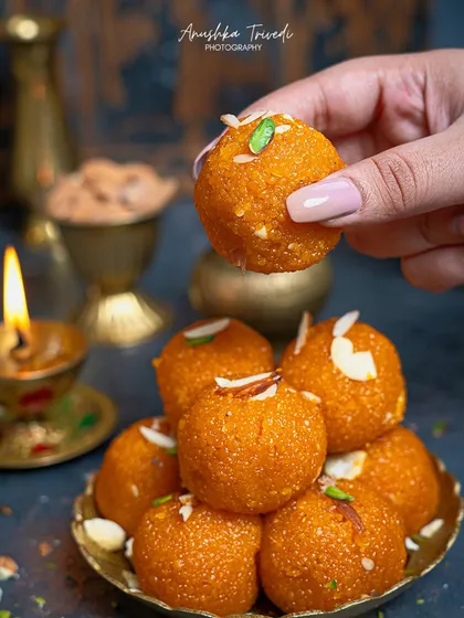 A hand reaching for a Motichoor Ladoo adds a dynamic and relatable element to the shot. It makes the viewer want to reach out and grab one too.