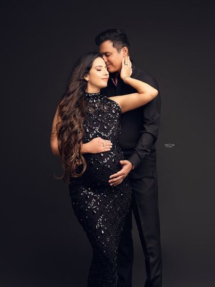 A glamorous and intimate couple's portrait against a dark background. The sequined black gown adds a touch of sparkle to this beautiful maternity moment.