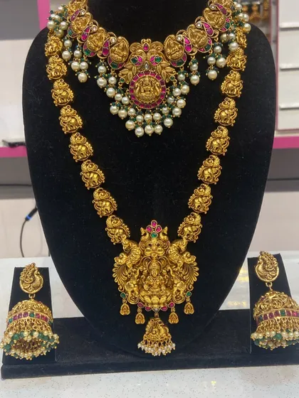 This full bridal set features two necklaces, a short one and a long haram, both with intricate Lakshmi pendants. The matching jhumkas complete the divine look.