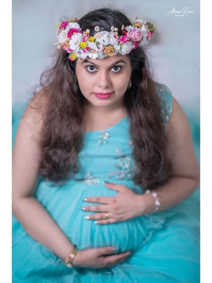 A close-up studio shot that focuses on the mother's direct gaze. The floral crown and elegant gown create a look that is both classic and beautiful.