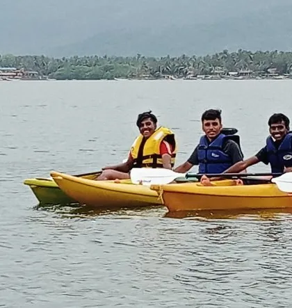 Three friends share a kayak, enjoying the calm waters and scenery during the summer camp in Karwar.