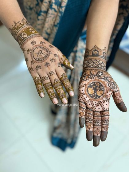 This Teej mehendi features different designs on each hand. One has the client's initials, while the other has a pair of swans in a central mandala, both celebrating love and partnership.