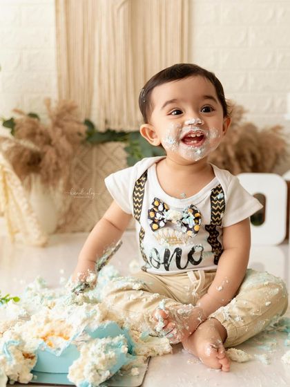 A full-body shot showing the happy aftermath of a cake smash, with cake crumbs and a smiling baby.