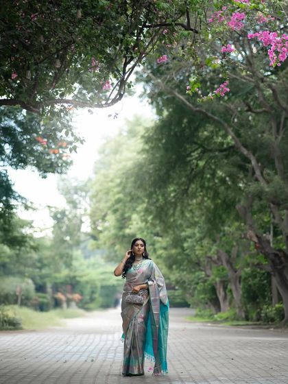 A wide shot showing the model walking down a tree-lined path, the saree's pallu trailing elegantly behind her.