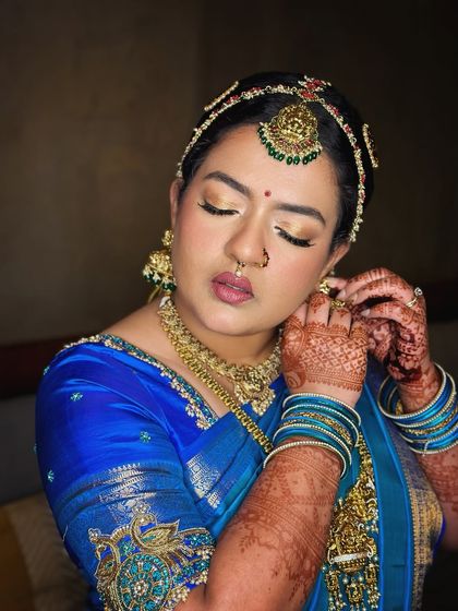 A candid moment of the bride adjusting her earring, highlighting the beautiful gold shimmer on her eyelids.