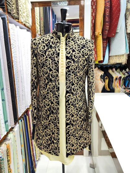 A black velvet open sherwani with all-over gold embroidery, displayed in the studio. This piece combines traditional motifs with a modern silhouette.