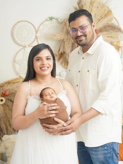 A happy family portrait in our boho studio. The parents hold their newborn son, who is wrapped in a cozy brown swaddle that complements the earthy, neutral tones of the set.
