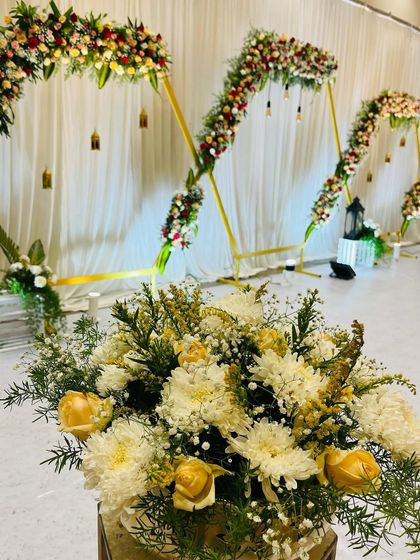 A detailed shot of a modern engagement stage. The hexagonal arches are decorated with flowers, and the foreground features beautiful floral arrangements in brass vases.