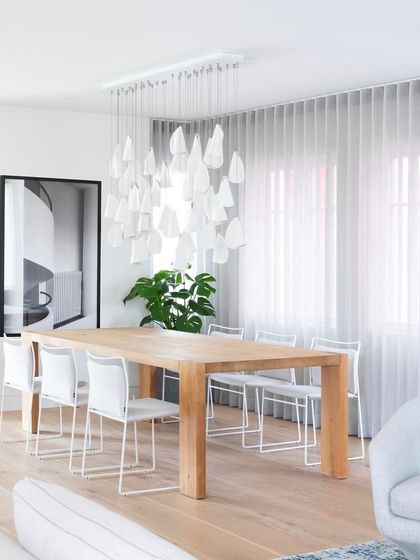 A rectangular canopy of Bocci 21 pendants hangs over a large wooden dining table in a bright, modern home.