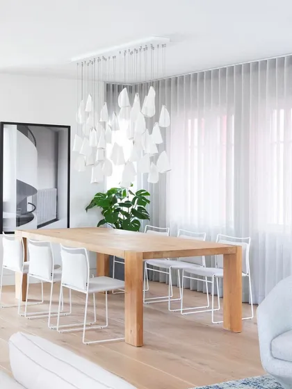 A rectangular canopy of Bocci 21 pendants illuminates a modern dining area. This linear arrangement provides excellent functional light while maintaining a soft, artistic aesthetic.