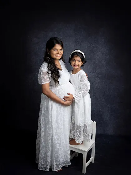 A beautiful mother-daughter portrait during a maternity session. They are wearing matching white lace dresses, creating a sweet and coordinated look that celebrates their bond.