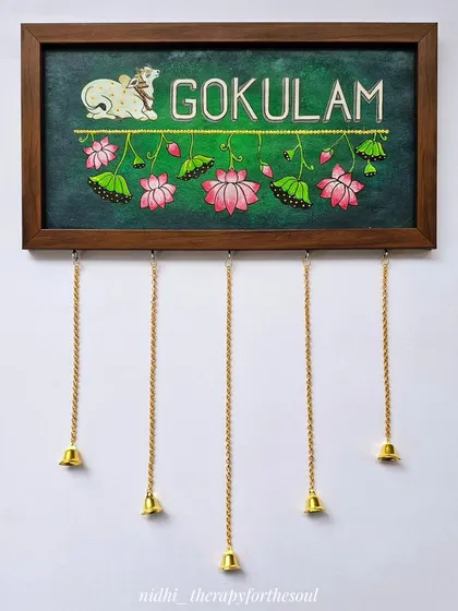 This 'Gokulam' nameplate is one of my favorites, featuring a serene Pichwai cow and inverted lotuses. The hanging brass bells add a lovely traditional touch and a gentle sound.