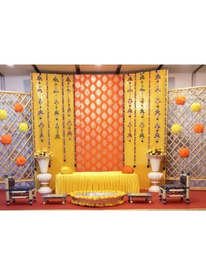 Here is a complete Haldi ceremony stage setup available for rent. It features traditional brocade fabric backdrops, decorative jaali panels, low seating (bajots), and a central urli for the rituals, all coordinated for a beautiful, traditional look.