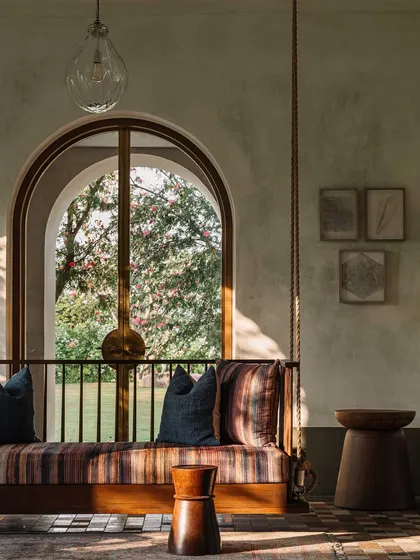 A traditional Indian swing or 'jhula' offers a place for relaxation while looking out onto the garden. This element combines cultural familiarity with modern design, framed by the home's signature arches.