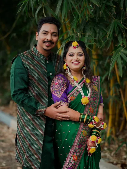 A lovely couple portrait from their Haldi day. They are dressed in matching green outfits, standing together against a natural bamboo backdrop, smiling happily for the camera.