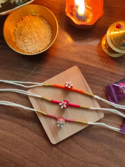These delicate floral rakhis are handmade with thread and small beads. They come in a variety of warm colors like orange, pink, and red.