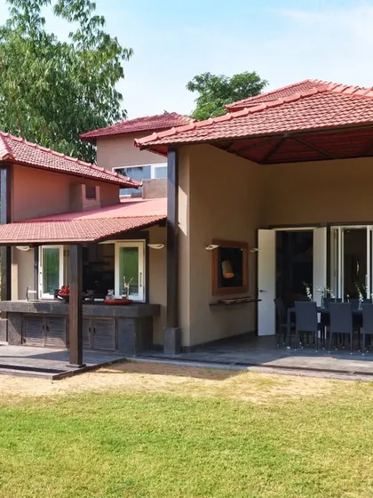 A side view of the Aishbagh home, revealing how the structure's silhouette and earthy tones harmonize with the landscape. The design uses covered verandas to create functional outdoor spaces for dining and relaxation.