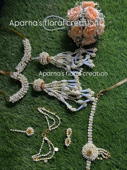 A baby shower jewellery set made with white buds and peach-colored roses. The set includes a floral bouquet, bajuband, and other matching pieces.