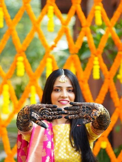 The bride proudly showing off her intricate Mehendi design. The vibrant orange marigold backdrop makes the deep color of the henna pop.