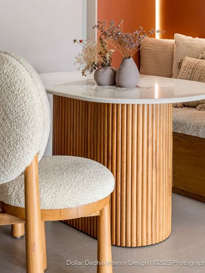 A close-up of the dining area details. The fluted wooden base of the table and the textured boucle chair add layers of tactile interest to the clean, modern design.