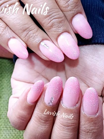 A soft pink glitter fade on almond-shaped nails, accented with a few delicate rhinestones.