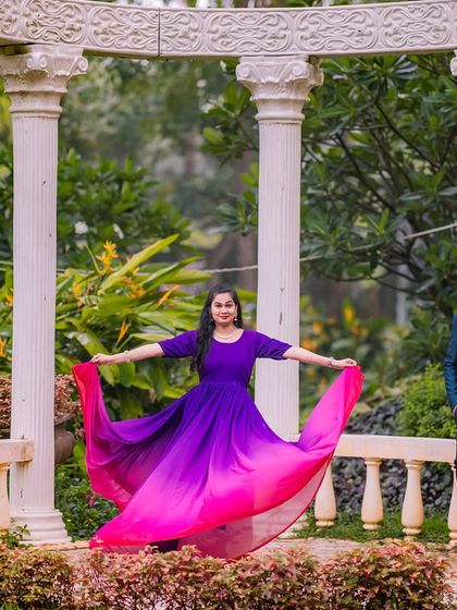 A woman in a flowing purple and pink dress poses at the white colonnade in the garden.