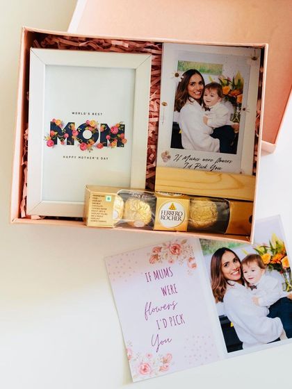 A Mother's Day hamper featuring a 'World's Best Mom' photo frame, a personalized wooden photo stand, and Ferrero Rocher chocolates, all in a lovely pink gift box.