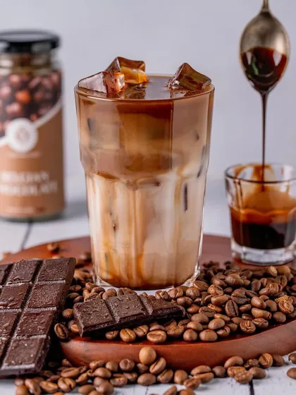 A rich and decadent iced coffee made with Belgian Chocolate flavor. The dripping chocolate syrup and surrounding coffee beans create a sensory experience, perfect for chocolate and coffee lovers.