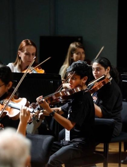 The violin section, a mix of our students and professional orchestra members, plays in unison. These collaborations are crucial for developing the listening skills and precision required for high-level ensemble performance.