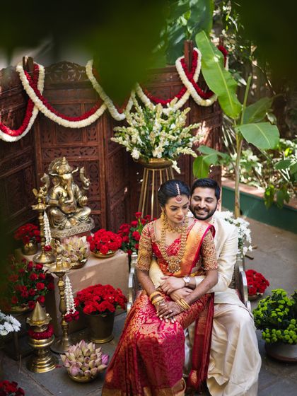 A couple seated before a Ganesha idol. Their traditional red and cream outfits were designed to be perfect for auspicious occasions and religious ceremonies.