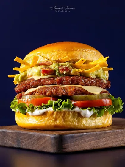 A fully loaded double-patty burger for Smasher Burgers by Chili's. This hero shot is styled to look tall and abundant, focusing on the layers of fresh ingredients, melted cheese, and crunchy toppings for a compelling menu photograph.
