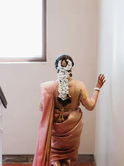 A back shot of a South Indian bride walking up the stairs, showcasing her traditional hairstyle adorned with a beautiful floral arrangement.