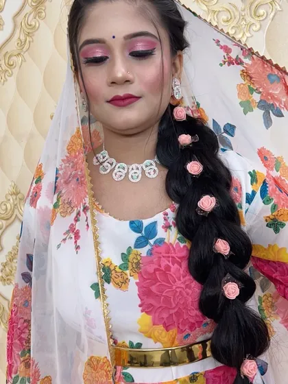 A lovely look for a daytime event, featuring a long, thick braid decorated with small pink roses. The makeup is fresh and pretty, with a focus on pink tones.