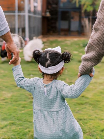 A little girl holding her parents' hands while exploring a farm. A sweet moment of guidance and discovery.