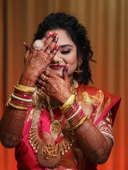 A playful and shy pose from a real bride, her hands adorned with intricate henna, covering her smiling face.