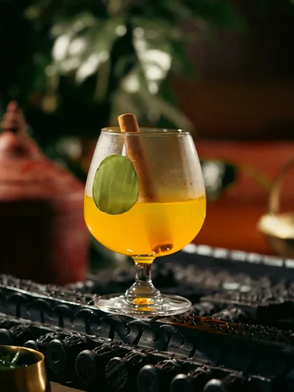 A warm, spiced cocktail with a cinnamon stick garnish. The dark, moody lighting creates a cozy and inviting feel.