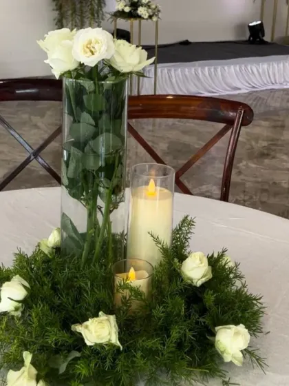 An elegant and simple centerpiece for the corporate event, featuring white roses and fresh greenery with flameless candles for a safe and classic look.