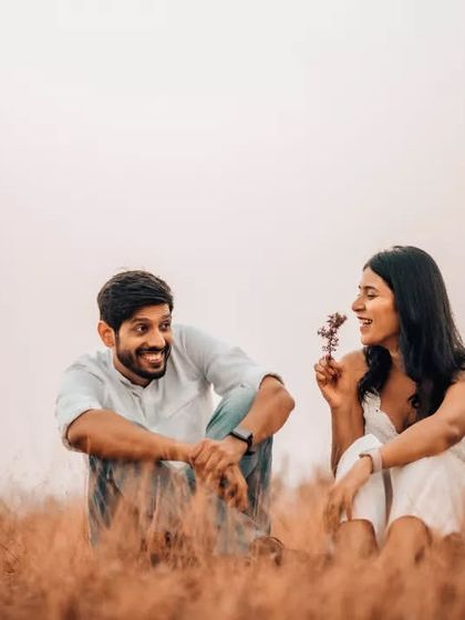 A playful and sweet interaction between a couple sitting in a rustic field. These unposed, lighthearted moments make for the most memorable pre-wedding photographs.